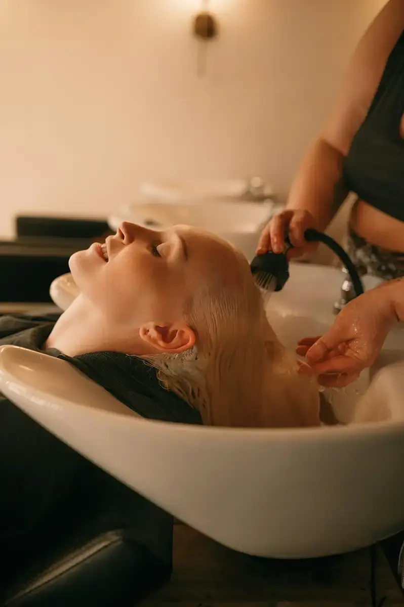 En person som ligger tillbakalutad vid en salongsvask medan en stylist tvättar håret med en handhållen duschmunstycke.